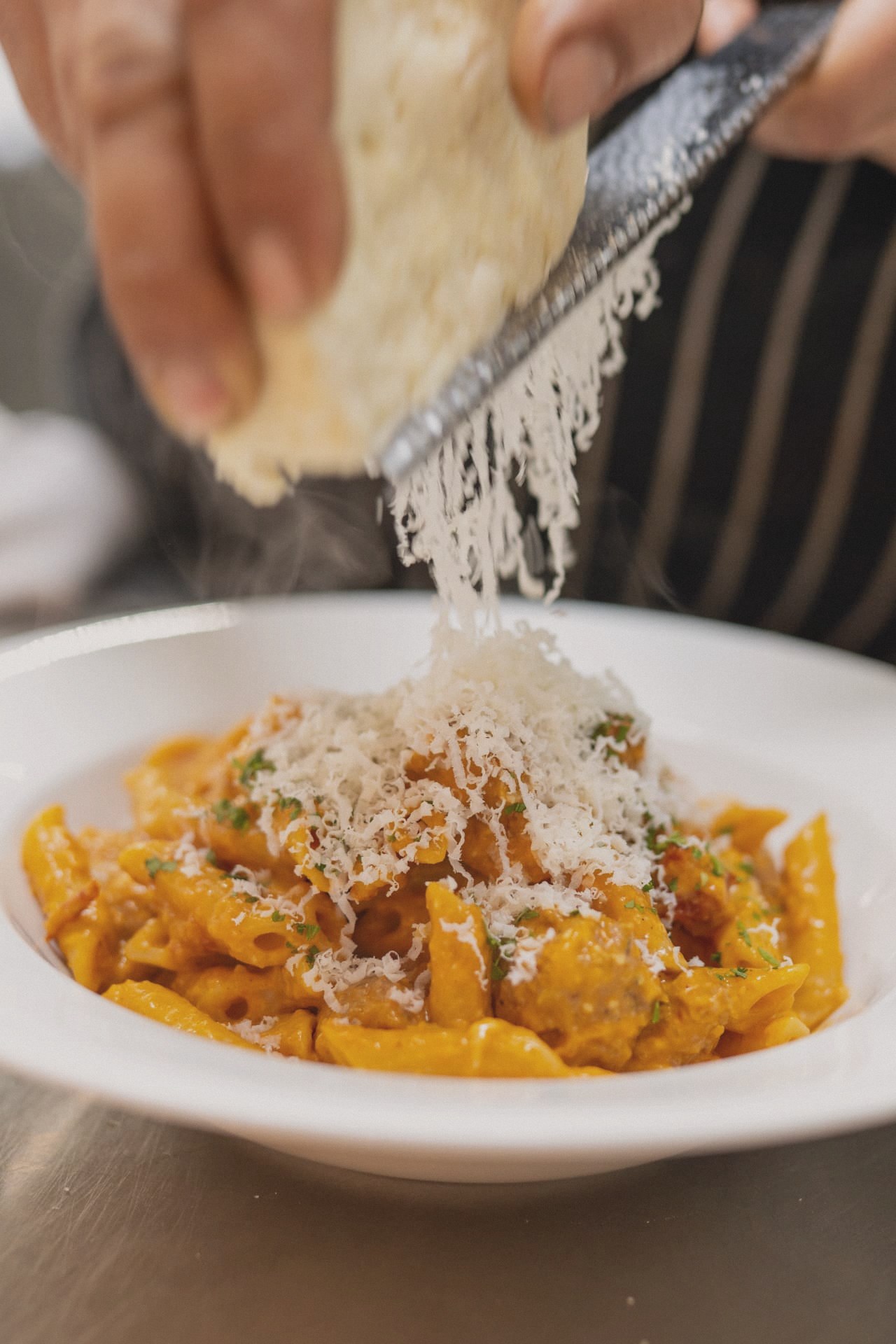 Parmesan grated over a bowl of creamy sausage penne in the kitchen