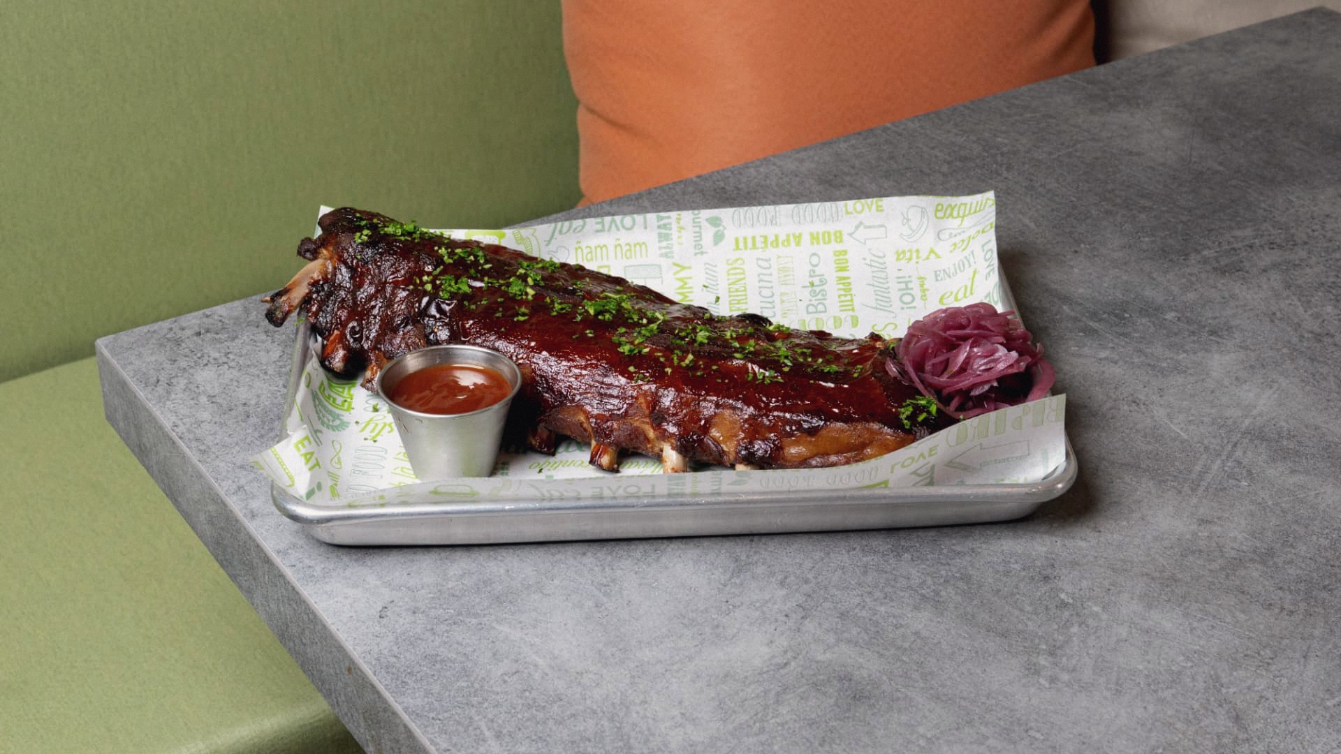 A full rack of smoked pork ribs on a tray with house barbecue sauce and pickled onions