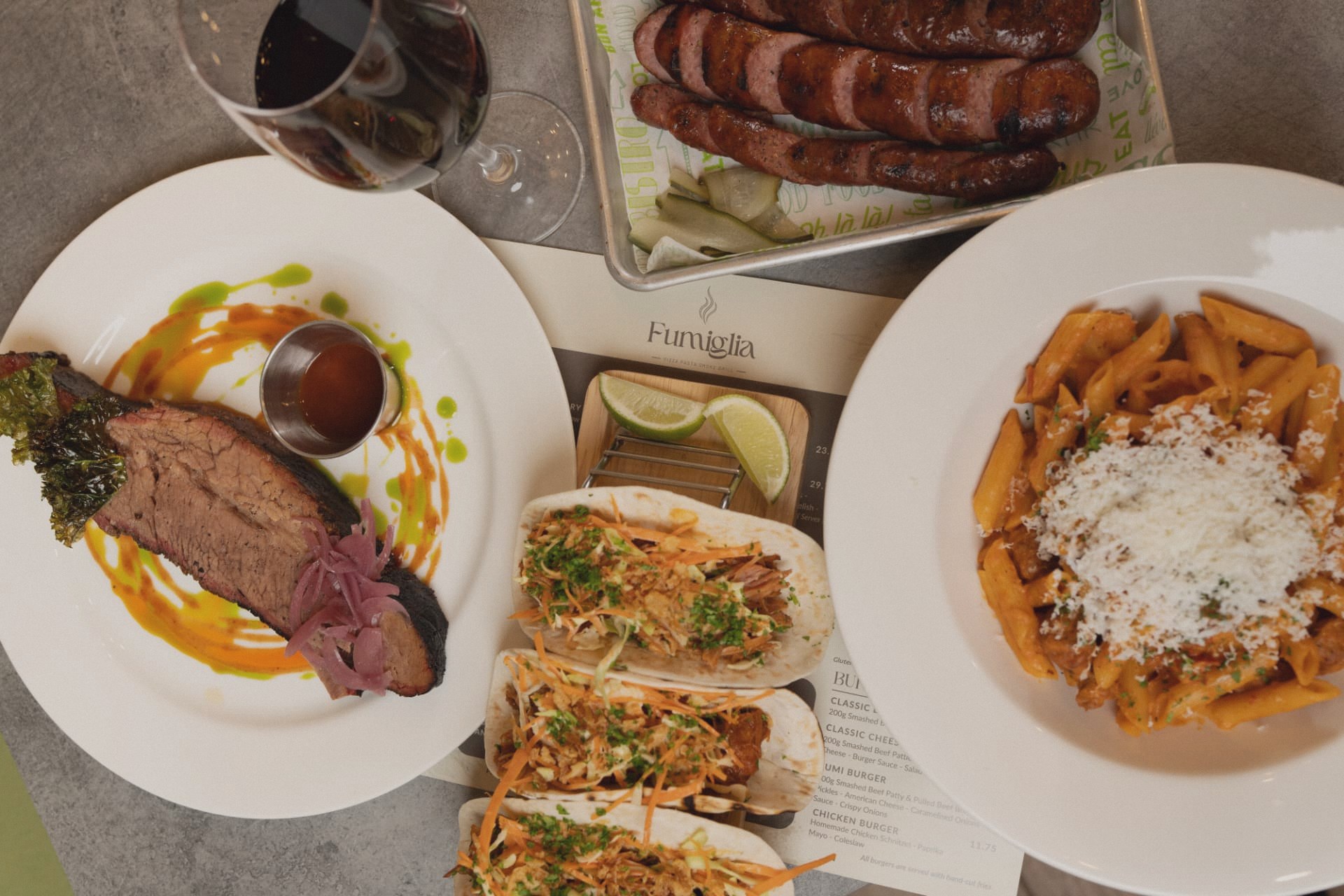 An overhead feast of smoked brisket, sausage, tacos, penne and red wine
